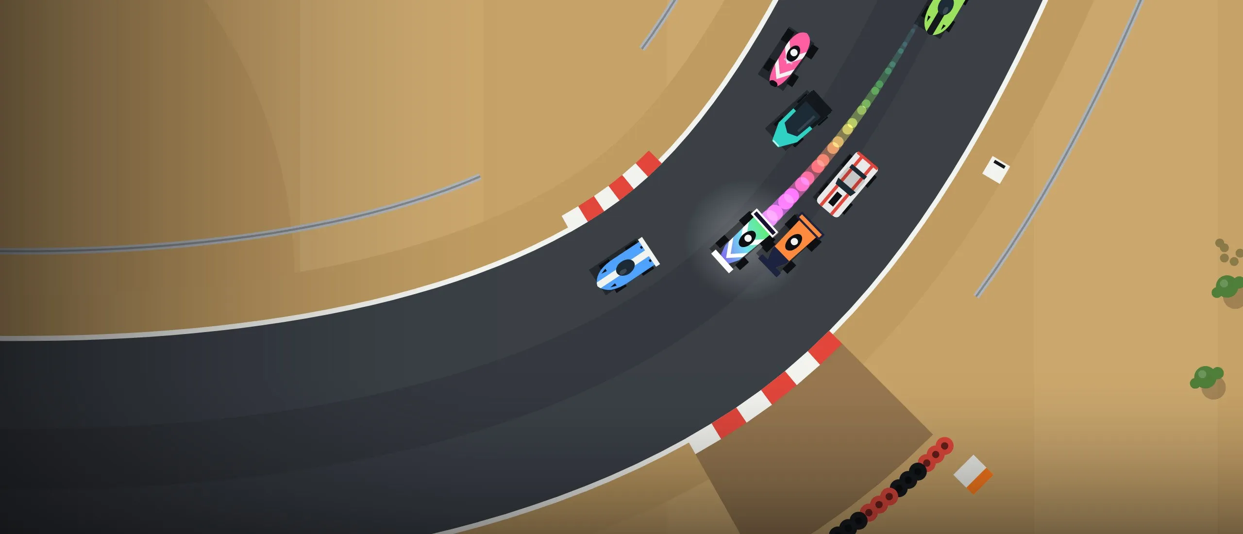 Top-down view of a pack of colourful race cars sweeping through a desert corner past red-and-white kerbs and a tyre wall, the lead car trailing a rainbow.